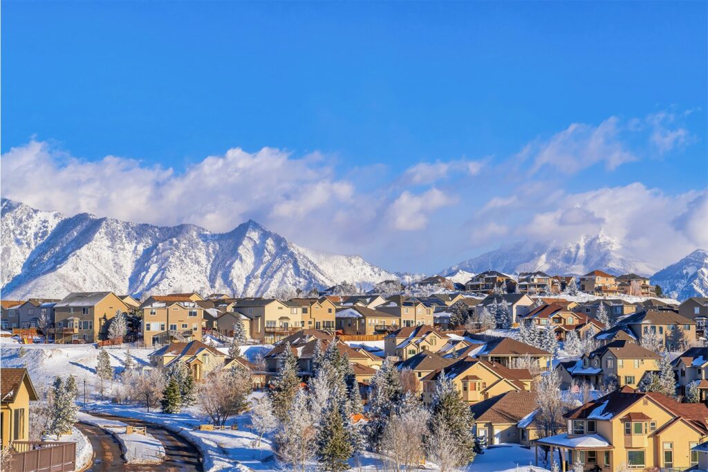 Snow-covered mountains and houses under a clear blue sky with clouds.