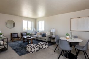 The room is furnished with a sofa and chairs around a table set for dining, all under artificial lighting from ceiling fixtures.